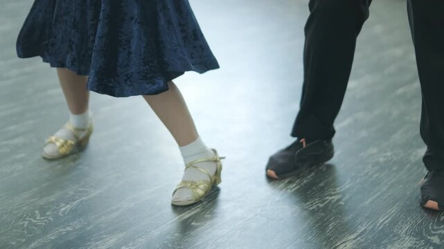 Child dancer's feet in golden high heel shoes training on a parquet floor during choreography lesson.