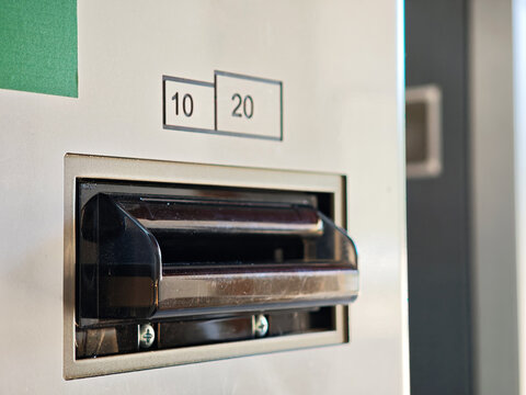 Close-up of a cash intake slot on a vending machine with 10 and 20 banknote denomination labels, black bill acceptor detail on beige payment terminal, electronic cash payment interface, no people