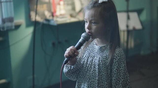 Little girl singing into a microphone during a vocal lesson with a teacher in a music studio.