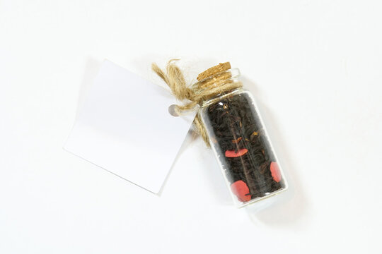 Small corked glass vial filled with loose leaf fruit tea tied with natural twine and blank white gift tag, isolated on white background, minimalist herbal packaging mockup in top view, no people