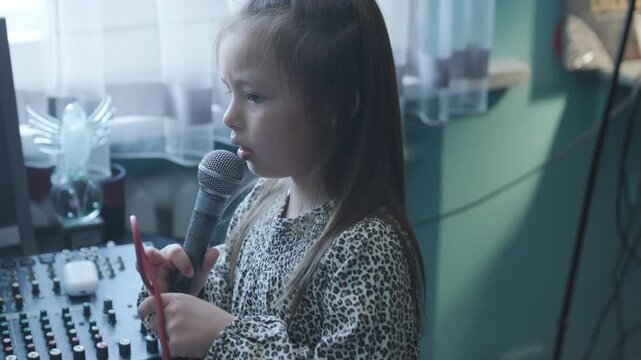 Little girl singing into a microphone during a vocal lesson with a teacher in a music studio.