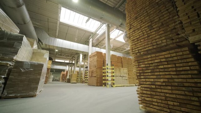 A large industrial warehouse featuring a forklift operating among stacks of dried wooden planks prepared for further furniture or flooring production