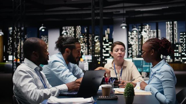 Manager gathering employees in office, evaluating staff performance using tablet, offering task completion feedback. Team leader oversees work done by multiethnic team, reviewing metrics.
