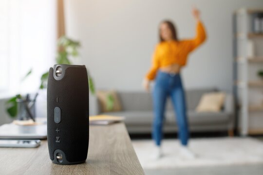 Joyful And Energetic Vibe. Unrecognizable Young Woman Dancing At Home While Enjoying Music From Bluetooth Speaker On Table In Modern Living Room. Fun And Relaxation Concept.