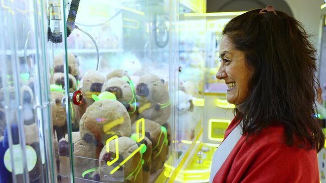 Excited woman laughing while playing a claw machine game in an arcade