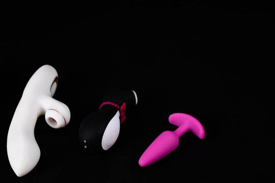 Three different adult sex toys including a white rabbit vibrator, a penguin suction stimulator, and a pink anal plug isolated on a black background.
