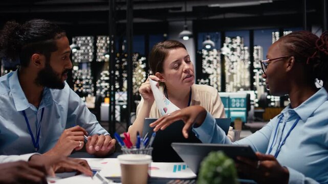 Looking over paperwork documents, diversity and team of employees in office late at night. Analyzing company budget and documentation files, coworkers cooperating on reports before deadline.