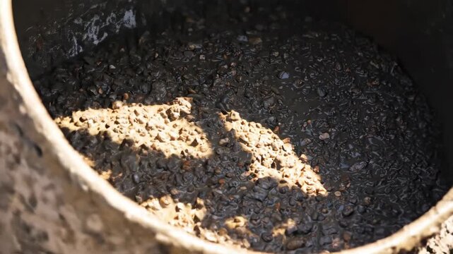 Sunbeams illuminate wet concrete mixture inside a rotating construction mixer, showcasing industrial building materials.