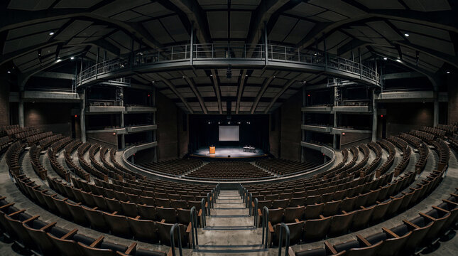 Extreme wide angle camera shot from back row inside massive dark empty university auditorium hall