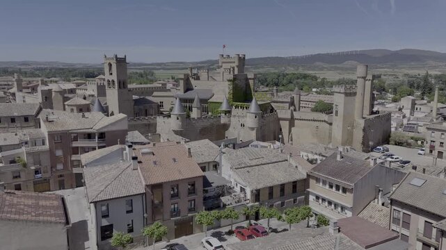 Aerial view flying low over town rooftops towards the Royal Palace of Olite Castle in Navarra, Spain. HDR/HLG drone shot of medieval architecture castle.