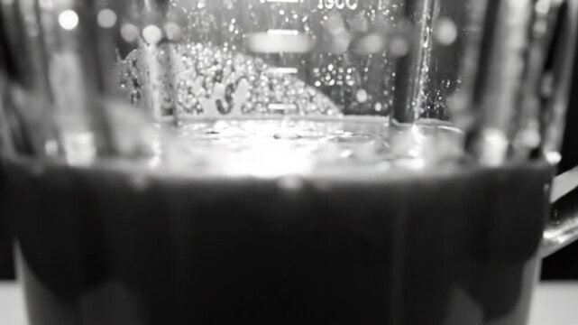 Black and white close up of a blender with a liquid inside reflecting and bubbling on a smooth surface