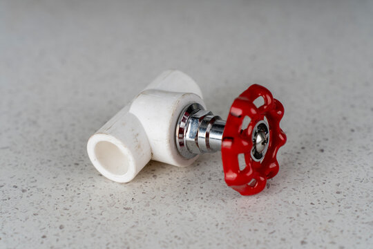 White polypropylene ppr pipe stop valve fitting with a red metallic round handwheel on a light speckled surface.