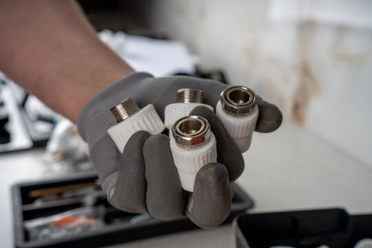 Hand in a grey protective glove holding four white polypropylene ppr plumbing adapters with integrated metal threaded connections.