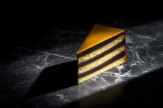 Slice of Dobos Torte on Dark Marble Surface with Dramatic Lighting and Shadow Play