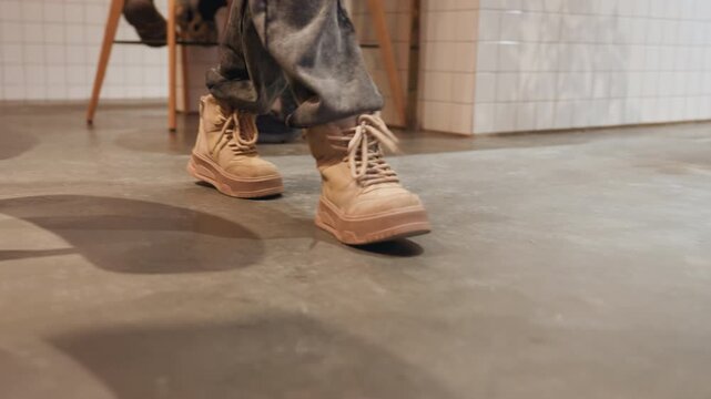 Cafe floor low shot of boots. Multiple customers crossing under tables with brisk steps and overlapping shadows, barista carrying tray, courier weaving past chairs, concrete and tile floor, brick