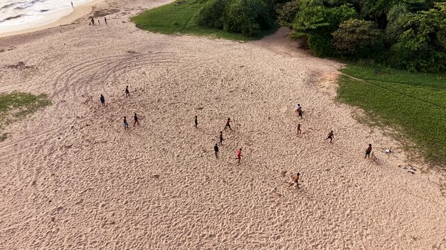 Aerial view of people playing football on a sandy beach bordered by lush tropical vegetation and the ocean Galle, Southern Province, Sri Lanka.