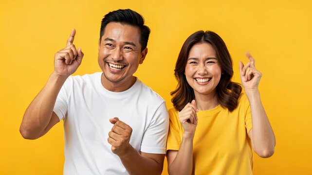 Optimism Personified: A joyful Asian couple, radiating happiness, crosses their fingers for good luck, their faces lit up with hope and anticipation against a vibrant yellow backdrop.