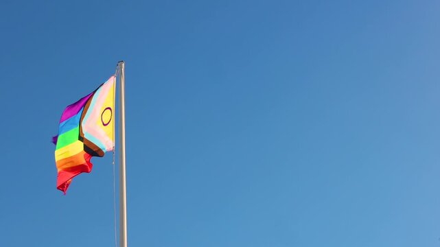 Rainbow pride flag waving in wind against blue sky LGBT equality symbol