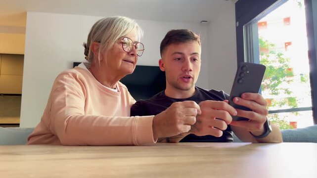 A young man and his grandmother happily use a smartphone together at home, fostering intergenerational connection, learning, and support.