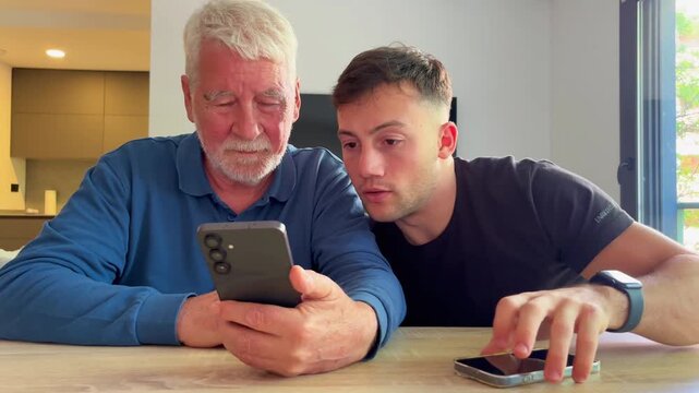A young man teaches an older man how to use his smartphone, demonstrating modern technology and intergenerational learning at home.
