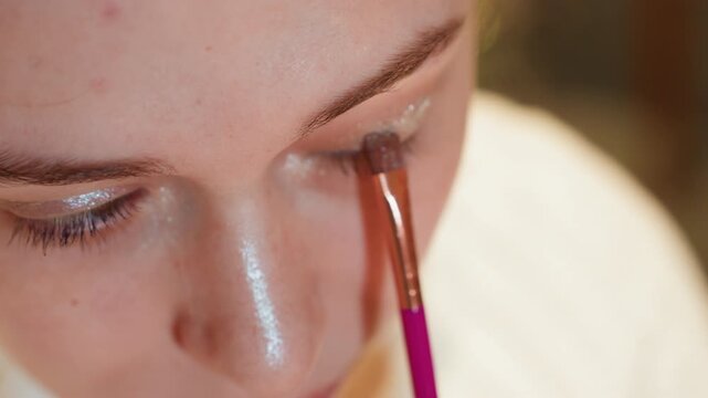 Closeup eye makeup application soft glam, focused brush strokes across upper eyelid, shimmering highlighter on nose bridge, natural skin texture, warm indoor lighting, calm preparatory mood, freelance