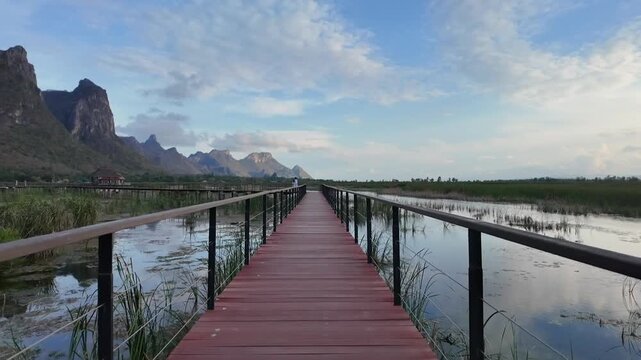 Wooden Boardwalk Over Watery Marsh with Mountain Backdrop: A long wooden boardwalk stretches over a calm, reflective marshland, leading towards a dramatic mountain range under a vast, cloudy sky.