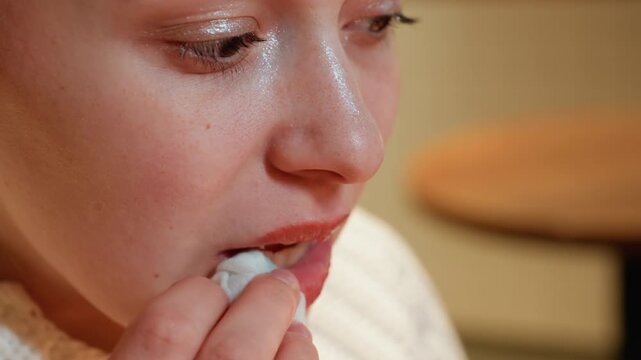 Closeup white woman testing balm in cafe, freelancer enjoying quick refresh chapstick application, subtle grin, mug and stool in background, cozy ambient light, candid expression