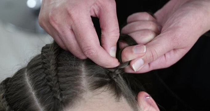 Hairstylist braiding teenage girl's hair in salon, closeup