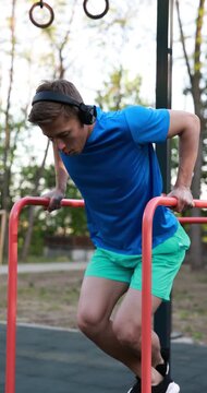 Athletic young man with headphones exercising on parallel bars at outdoor gym