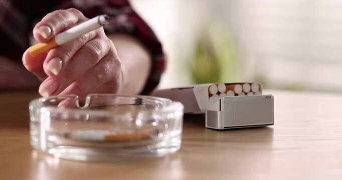 Woman flicking ash from cigarette into ashtray at wooden table, closeup