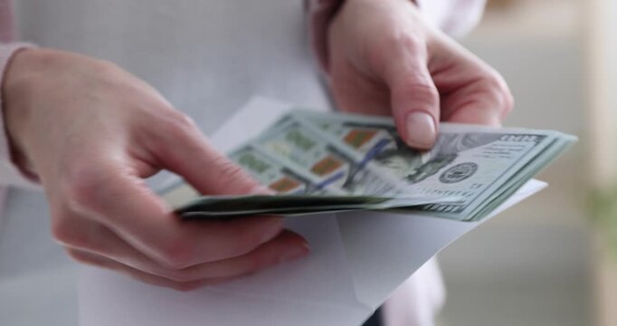 Woman opening envelope with dollar banknotes indoors, closeup