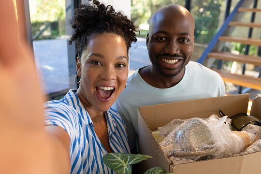 Couple posing at home, woman taking selfie holding smartphone, man holding box with lamp