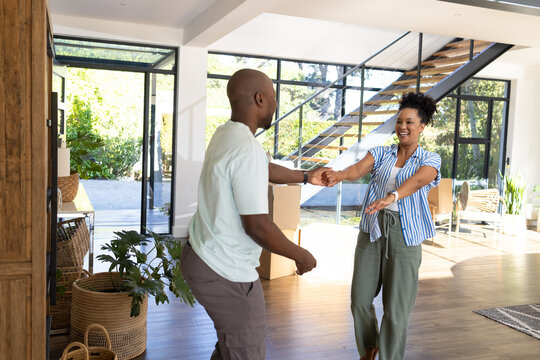 African American couple holding hands, moving into open-plan living room with moving boxes, plants