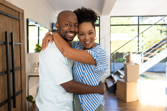 African American couple embracing, unpacking in modern living area with moving boxes and smartwatch