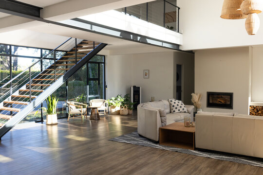 Beige sofas gathering around low coffee table in open-plan living area, glass wall revealing garden