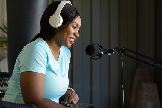 Woman wearing white headset and light blue shirt smiling while leaning toward black mic at studio