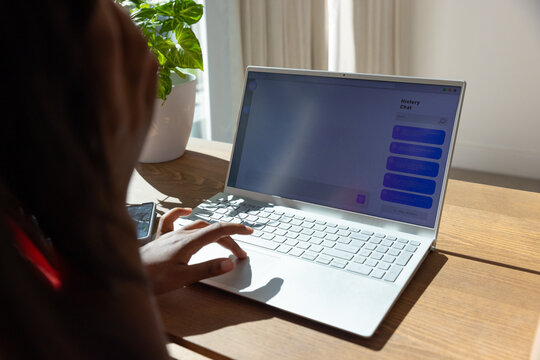 African American woman wearing red top typing on laptop at desk with smartphone, plant, copy space