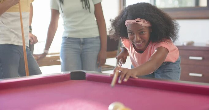 African American friends playing, woman in pink shirt lining up, striking cue on magenta pool table