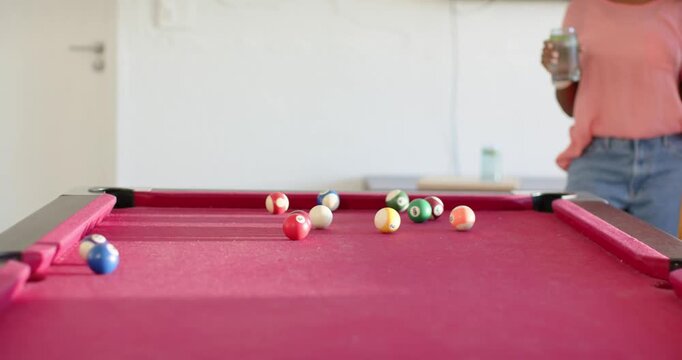 Diverse friends hitting cue, sending balls rolling on pool table in rec room holding jars playing