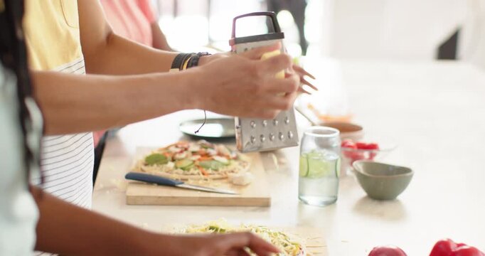 African American friends starting topping pizzas, grating with box grater in kitchen for meal