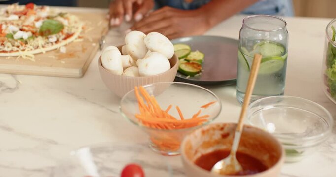 African American friends making pizza on counter after prep, adding mushrooms and sauce for dinner