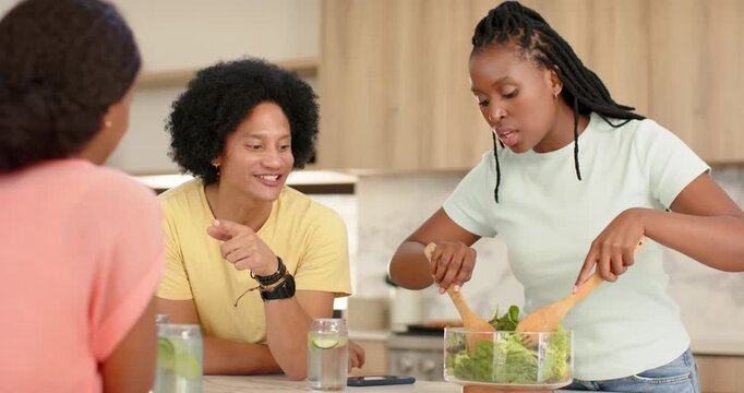 African American women meeting at kitchen island woman tossing salad in glass bowl, making food