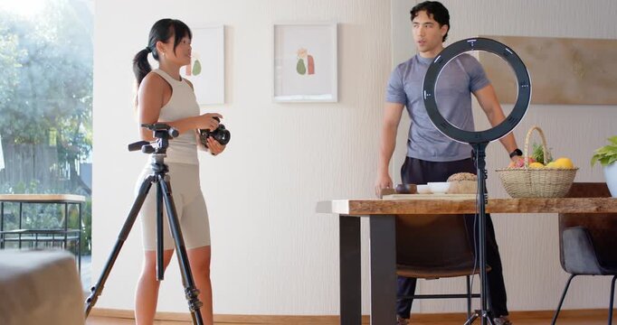 Diverse collaborators photographer pointing, directing man posing at home by ring light for shoot
