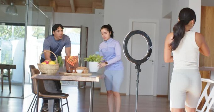 Diverse friends following photog gestures arranging plant by ringlight for at home shoot in gymwear