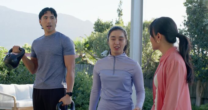 Diverse friends on patio centered woman in lavender introducing friend, man shifting kettlebells