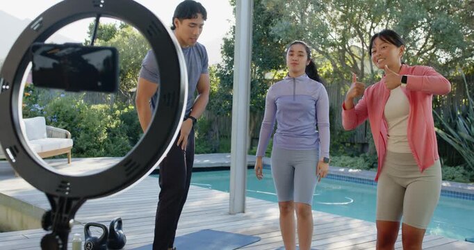 Diverse friends in sportswear prompted by ringlight filming workout on pool deck, stepping, smiling