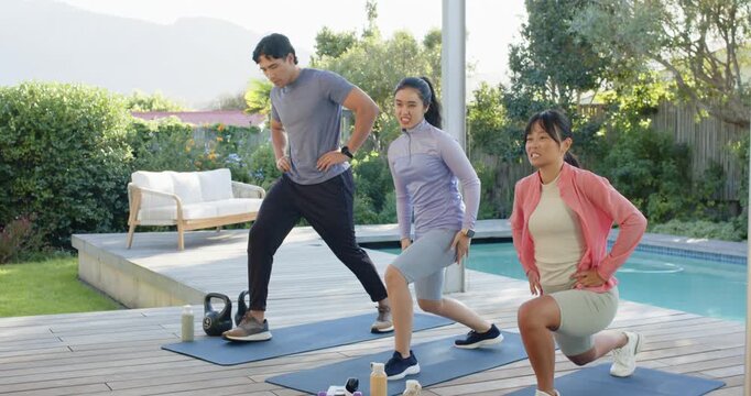 Diverse friends starting hands-on-hips, doing lunges in sync on backyard pool deck with blue mats