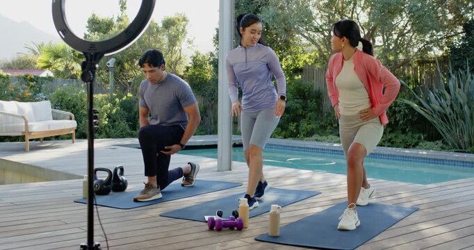 Diverse instructor stepping between mats guiding two clients doing lunges on pool deck fixing form