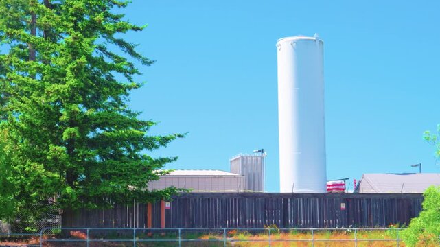 Large white vertical industrial storage silo tank behind wooden fence