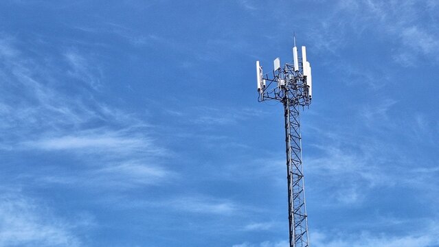 Cellular Communication Tower Against Blue Sky with Wispy Clouds and Modern Technology